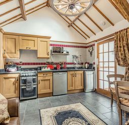 A kitchen with wooden cabinets a stove dishwasher and dining table with chairs at Y Becws in Llanbedr near Harlech