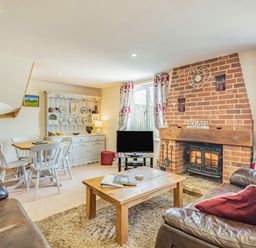 A living room with a wood burning stove fireplace a wooden coffee table leather sofas a dining table with chairs and a white cabinet at Harvest Moon in Grundisburgh