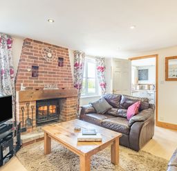 A living room with a brick fireplace a wooden coffee table two leather sofas and a television at Harvest Moon in Grundisburgh