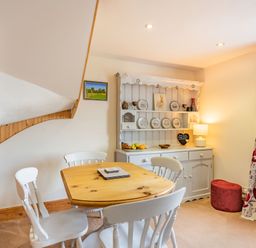 A dining area with a wooden table and white chairs next to a white dresser with plates and a lamp at Harvest Moon in Grundisburgh