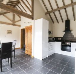 A kitchen and dining area with a glass table black chairs white cabinets and wooden beams at Jackos Barn in Homersfield