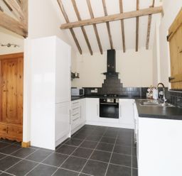A kitchen with white cabinets black countertops wooden beams on ceiling and black tile floor at Jacko's Barn in Homersfield