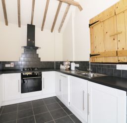 A kitchen with white cabinets black countertops black tiled backsplash wooden wall cupboards and exposed ceiling beams at Jacko's Barn in Homersfield