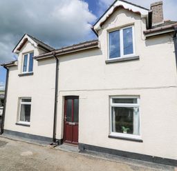 The exterior of a two story house with white walls a brown front door and multiple windows at Green Cottage in Pant-y-Dwr near Rhayader