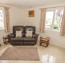 A living room with a brown leather sofa two patterned cushions two wooden tables and a small electric fireplace at Lawn Lodge in Ashleworth