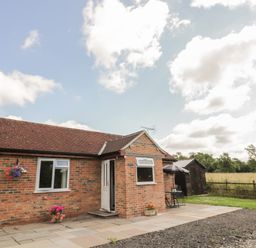 A single-story brick house with a tiled roof and white door in a rural setting with a patio and garden furniture at Lawn Lodge in Ashleworth