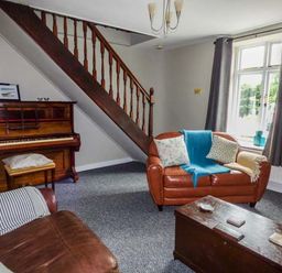 A living room with a piano brown sofas a wooden chest and a window with dark curtains at Corner Cottage Reynoldston near Swansea