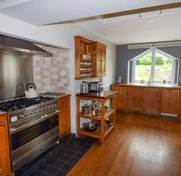 A kitchen with wooden cabinets a stainless steel stove and oven a window with a garden view at Corner Cottage in Reynoldston near Swansea