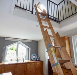 A wooden ladder leading to a loft opening in a kitchen with wooden cabinets and windows at Corner Cottage in Reynoldston near Swansea