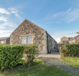 Stone cottages with trimmed bushes and gravel path under blue sky at Long Cart Cottage in Embleton