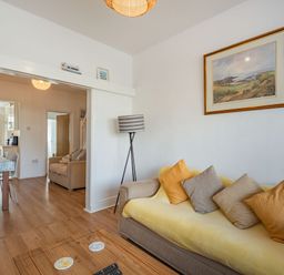 A living room with a sofa and cushions adjacent to a dining area with a table and chairs at 2 Tregof Terrace in Cemaes Bay