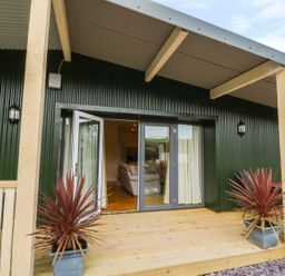 A wooden porch with potted plants in front of glass doors leading to a living room at Y Felin - Moana in Borth near Aberystwyth