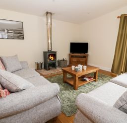 A living room with two sofas a coffee table a wood stove and a television at Y Felin - Moana in Borth near Aberystwyth