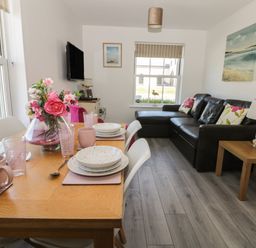A dining table set with plates and cups and a vase of flowers next to a living room with a leather sofa and a side table with a lamp at White Rose Apartment in Filey