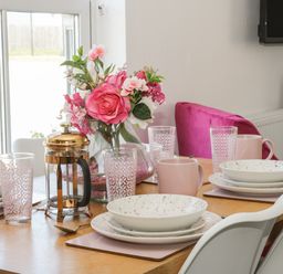 A dining table set with plates mugs glasses and a flower vase at White Rose Apartment in Filey