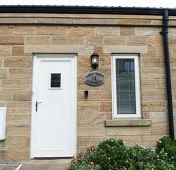 Exterior view of a stone cottage with a white door and window a lamp and garden in front at Kingfisher in Whitby