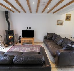 A living room with two black leather sofas a wood burning stove a wooden coffee table with a television and framed pictures on the wall at Kingfisher in Whitby