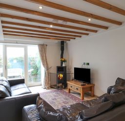 A living room with two brown leather sofas a wooden coffee table with a TV a fireplace with flowers on top and glass doors leading outside at Kingfisher in Whitby