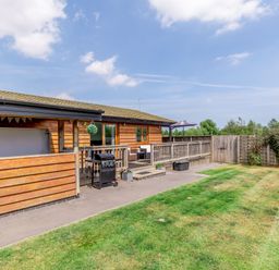 A wooden house with a patio grill and outdoor seating in a fenced garden at Kingfisher Lodge in Brandesburton