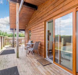 A wooden deck with outdoor chairs and tables next to sliding glass doors at Kingfisher Lodge in Brandesburton