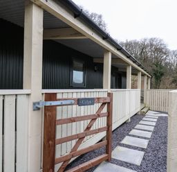 A wooden gate with a sign that reads Celyn leading to a covered porch with a set of concrete stepping stones at Y Felin - Celyn in Borth