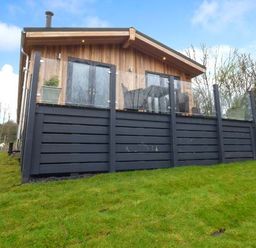 A wooden cabin with a black fenced porch and green grass in front at Crook Lodge in Allithwaite near Grange-over-Sands