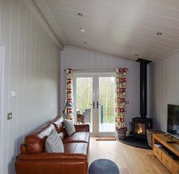 A living room with a leather sofa wood burning stove and television at Crook Lodge in Allithwaite near Grange-over-Sands