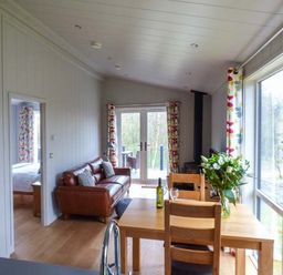 A dining table with chairs and flowers next to a sofa and glass doors in a living room at Crook Lodge in Allithwaite near Grange-over-Sands