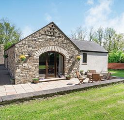 A stone and plaster cottage with patio furniture on a tiled terrace in a garden at Highbury in Spittal near Haverfordwest