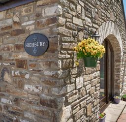 Stone exterior wall with a sign reading Highbury and hanging flower pots at Highbury in Spittal near Haverfordwest