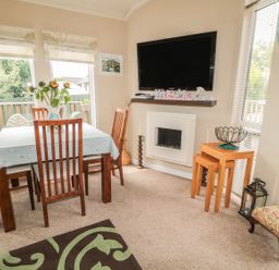 A dining area with a wooden table and chairs a television mounted on the wall a fireplace and side tables at Little Gem Lodge Charlesfield near St Boswells