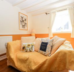 A living room with a sofa covered with yellow fabric and cushions by a window with white curtains at The Pound in Trellech near Monmouth