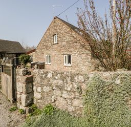 A stone house with three windows and a tiled roof behind a stone wall with plants and a wooden gate at The Pound in Trellech near Monmouth