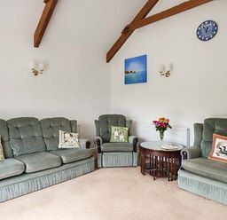 A living room with green upholstered sofa and chairs with pillows and a wooden round table with flowers at Shepherds Rest in Jacobstow near Bude