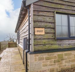 Exterior corner of a wooden building with stone base and a window with frosted glass and blinds at Coquet in Longframlington near Alnwick
