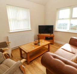 A living room with a brown sofa two armchairs a wooden coffee table with a bottle and two glasses and a television at Coquet in Longframlington near Alnwick