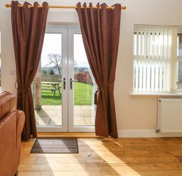 A room with brown curtains on glass doors leading to a garden and a brown sofa at Coquet in Longframlington near Alnwick