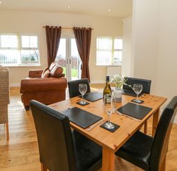 A dining table set with glasses and cutlery next to a living area with sofas and windows at Coquet in Longframlington near Alnwick