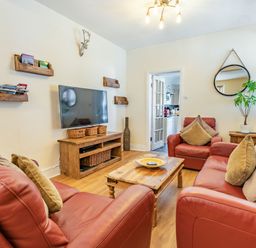 A living room with red leather sofas a wooden coffee table a wall-mounted tv and a round mirror at Dringarth in Tenby
