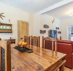 A dining area with a wooden table and chairs and a living room with red sofas and a TV at Dringarth in Tenby