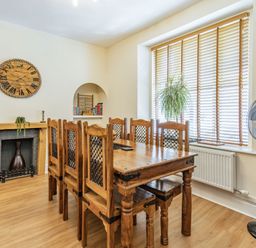 A dining room with a wooden table and chairs a large window with wooden blinds and a clock on the wall at Dringarth in Tenby