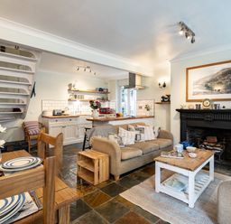 An open-plan living area with a kitchen, dining table, sofa, fireplace, and staircase at Cobble Cottage in Boscastle near Tintagel