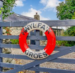 A wooden gate with a life ring attached and a stone building with plants behind at Hwylfa'r Groes in Talybont near Barmouth