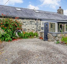 Exterior of a stone cottage with a gravel driveway and plants near the entrance at Hwylfa'r Groes in Talybont near Barmouth