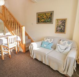 A living room with a wooden staircase a sofa with cushions a table with chairs and paintings on the walls at Bryn Melyn Artist's Cottage Llanelltyd near Dolgellau