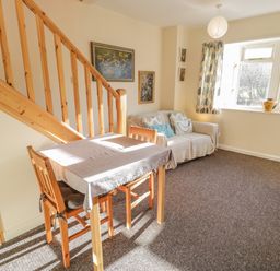 A living room with a wooden dining table and chairs near stairs and a sofa by a window at Bryn Melyn Artist's Cottage Llanelltyd near Dolgellau