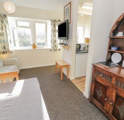 A living area with a sofa cushions and curtains a wooden cupboard and a wall mounted tv at Bryn Melyn Artists Cottage Llanelltyd near Dolgellau