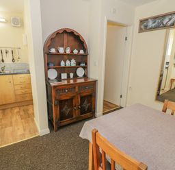 A dining area with a wooden table and chairs next to a kitchen with hanging utensils and a dark wooden cabinet at Bryn Melyn Artist's Cottage Llanelltyd near Dolgellau
