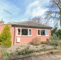 A brick house with two white framed windows and plants in front at The Lodge in Coltishall