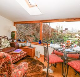 A living area with a sofa table lamp and glass dining table with four chairs by large windows at The Lodge in Coltishall